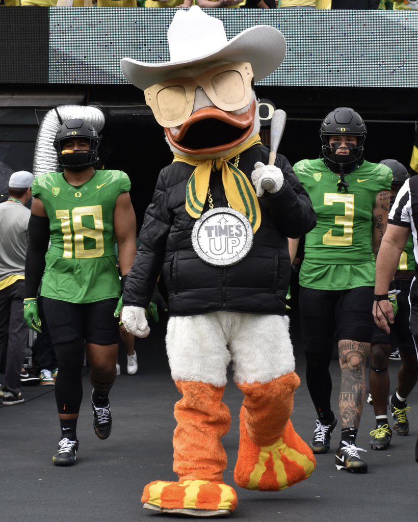 The Oregon Duck mascot leads the team out of the tunnel at Autzen Stadium wearing a cowboy hat and Time's Up chain